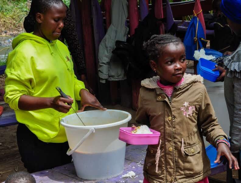 A volunteer serving food to a child during MaSCA's children's feeding program