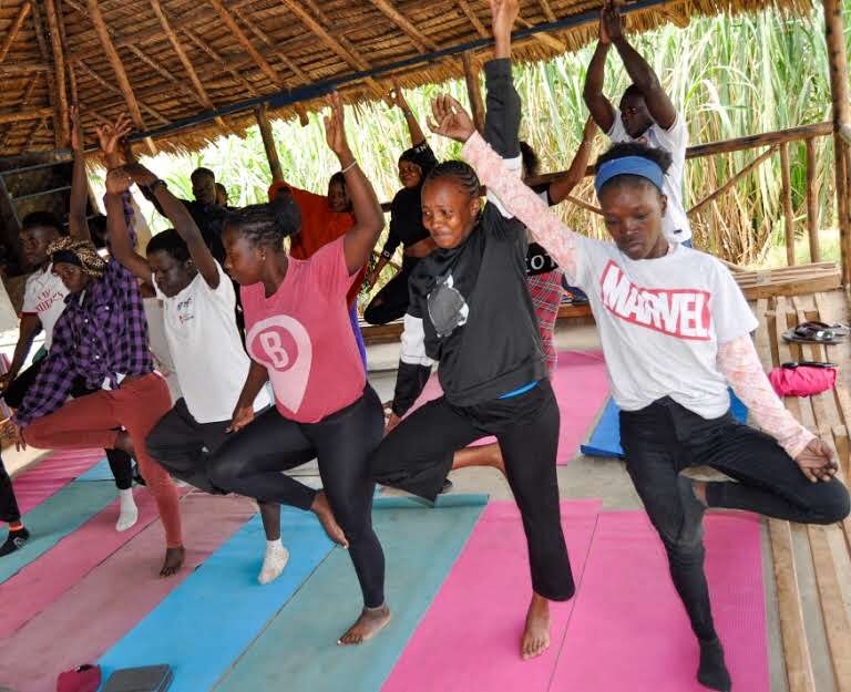 Community members practicing yoga together under a thatched shelter as part of MaSCA's wellness program